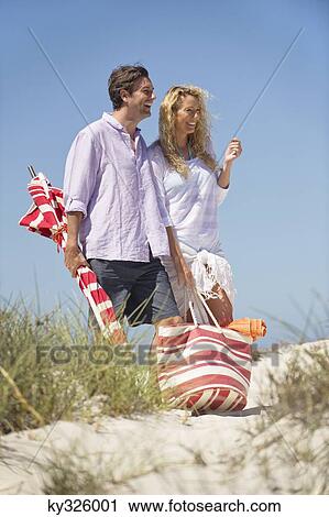 Stock Image - Mid adult couple walking on the beach. Fotosearch