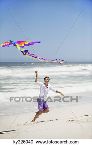 Mid adult man flying kite on the beach View Large Photo Image Stock Image - Mid adult man flying kite on the beach. Fotosearch