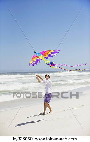 Stock Image - Mid adult man flying kite. Fotosearch