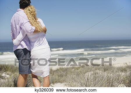 Stock Photo - Rear view of a couple looking at sea. Fotosearch