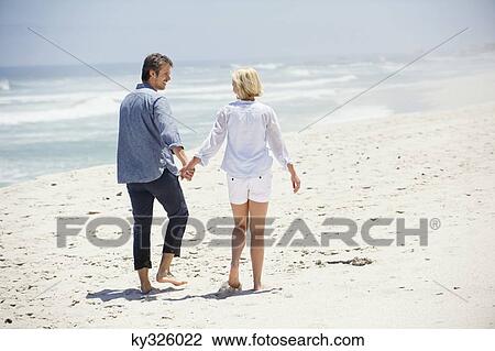 Stock Image - Rear view of a couple walking on the beach. Fotosearch