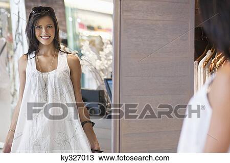 Portrait of a beautiful young woman trying on a dress in a mirror View Large Photo Image Stock Image - Portrait of a beautiful young woman trying on a dress in a mirror. Fotosearch