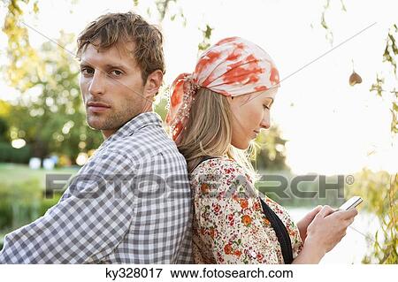 Man looking at camera while woman text messaging on a mobile phone View Large Photo Image Stock Photo - Man looking at camera while woman text messaging on a mobile phone. Fotosearch