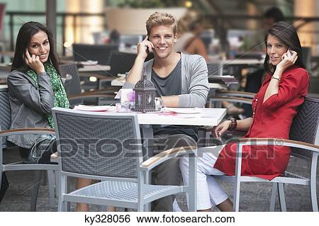 Three young friends talking on mobile phones in a restaurant View Large Photo Image Stock Photograph - Three young friends talking on mobile phones in a restaurant. Fotosearch