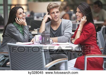 Three young friends talking on mobile phones in a restaurant View Large Photo Image Stock Photography - Three young friends talking on mobile phones in a restaurant. Fotosearch