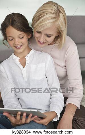 Picture - Woman assisting her daughter in using a digital tablet. Fotosearch