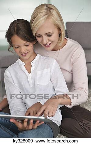 Stock Photo - Woman assisting her daughter in using a digital tablet. Fotosearch