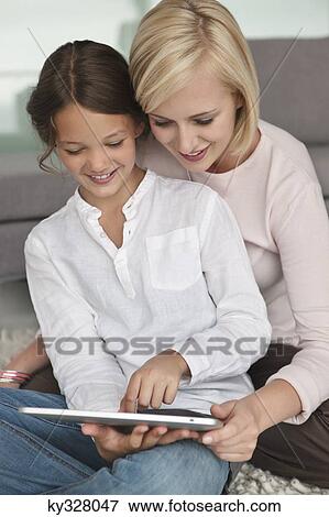 Woman assisting her daughter in using a digital tablet View Large Photo Image Stock Photo - Woman assisting her daughter in using a digital tablet. Fotosearch