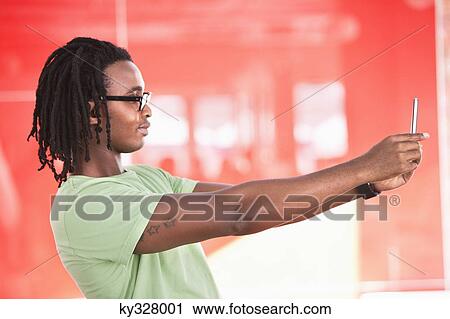 Stock Image - Young man taking a picture of himself with a mobile phone. Fotosearch