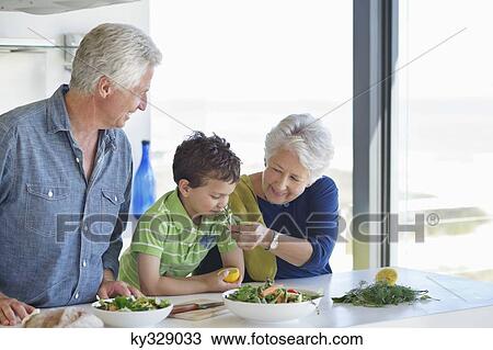 Boy smelling vegetable with his grandparent standing besides him in a kitchen View Large Photo Image Stock Image - Boy smelling vegetable with his grandparent standing besides him in a kitchen. Fotosearch