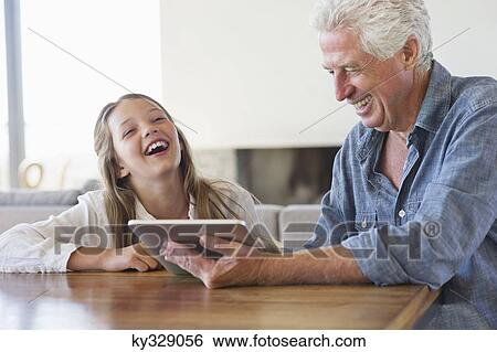 Stock Photograph - Girl laughing while her grandfather using a digital tablet. Fotosearch