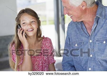 Girl talking on a mobile phone with her grandfather near her View Large Photo Image Stock Image - Girl talking on a mobile phone with her grandfather near her. Fotosearch