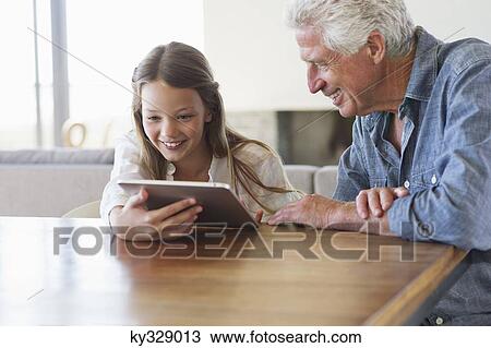 Girl using a digital tablet with her grandfather sitting near her View Large Photo Image Stock Image - Girl using a digital tablet with her grandfather sitting near her. Fotosearch