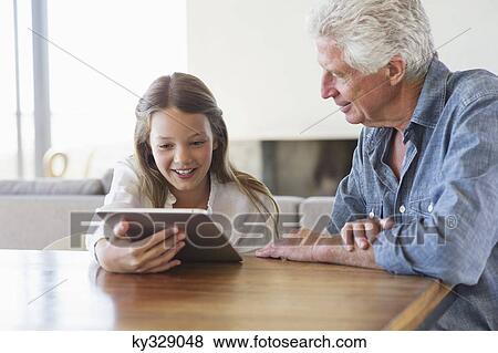 Girl using a digital tablet with her grandfather sitting near her View Large Photo Image Stock Photo - Girl using a digital tablet with her grandfather sitting near her. Fotosearch