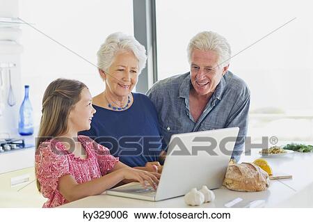 Girl using a laptop with her grandparents looking at her in a kitchen View Large Photo Image Stock Photograph - Girl using a laptop with her grandparents looking at her in a kitchen. Fotosearch