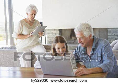 Man using a laptop with his granddaughter and his wife working on a digital tablet in background View Large Photo Image Stock Image - Man using a laptop with his granddaughter and his wife working on a digital tablet in background. Fotosearch