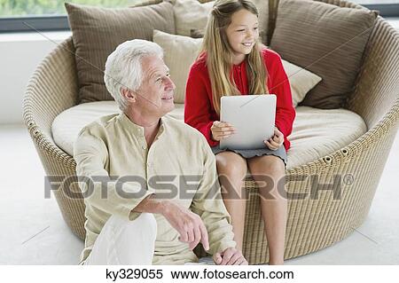 Senior man sitting with his granddaughter holding a digital tablet View Large Photo Image Stock Photography - Senior man sitting with his granddaughter holding a digital tablet. Fotosearch