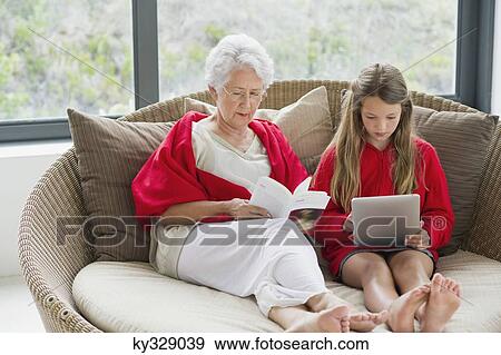 Stock Photo - Senior woman reading a magazine with her granddaughter using a digital tablet. Fotosearch