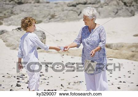 Senior woman with her grandson collecting shell on the beach View Large Photo Image Stock Photo - Senior woman with her grandson collecting shell on the beach. Fotosearch