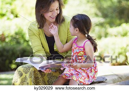 Stock Photo - Woman and her granddaughter looking at each other while holding a book in hand. Fotosearch