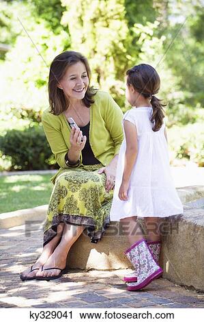 Stock Image - Woman holding a mobile phone and looking at her granddaughter. Fotosearch
