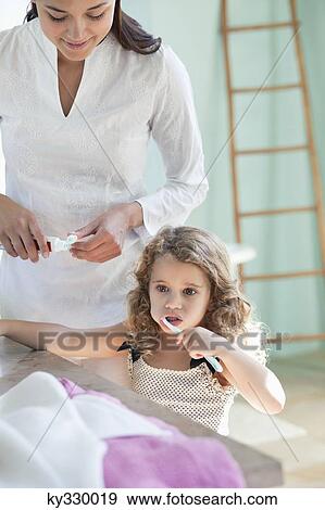 Cute little girl brushing teeth while mother looking at her View Large Photo Image Stock Photo - Cute little girl brushing teeth while mother looking at her. Fotosearch