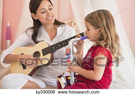Woman playing guitar with her daughter playing saxophone View Large Photo Image Stock Photograph - Woman playing guitar with her daughter playing saxophone. Fotosearch