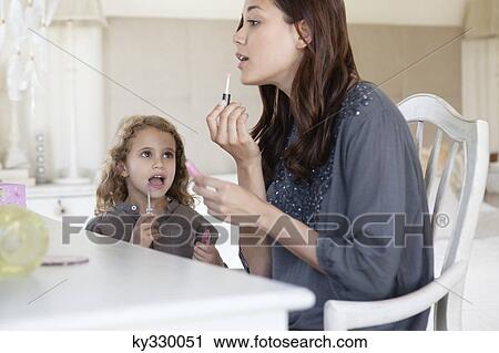Young woman and little girl applying lip gloss at dressing table View Large Photo Image Stock Image - Young woman and little girl applying lip gloss at dressing table. Fotosearch