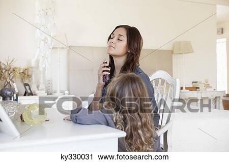 Stock Image - Young woman applying perfume while her daughter beside her. Fotosearch