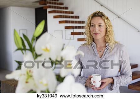 Beautiful mid adult woman holding coffee cup and looking at flowers View Large Photo Image Stock Photo - Beautiful mid adult woman holding coffee cup and looking at flowers. Fotosearch