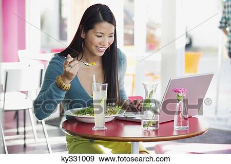 Beautiful woman eating food while looking at laptop in a restaurant View Large Photo Image Stock Photo - Beautiful woman eating food while looking at laptop in a restaurant. Fotosearch