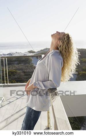 Stock Image - Mid adult woman leaning against a balcony. Fotosearch