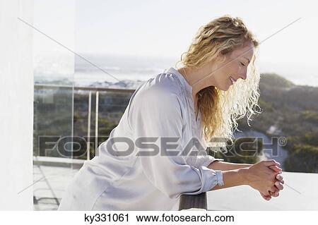 Mid adult woman standing at a balcony and smiling View Large Photo Image Stock Image - Mid adult woman standing at a balcony and smiling. Fotosearch