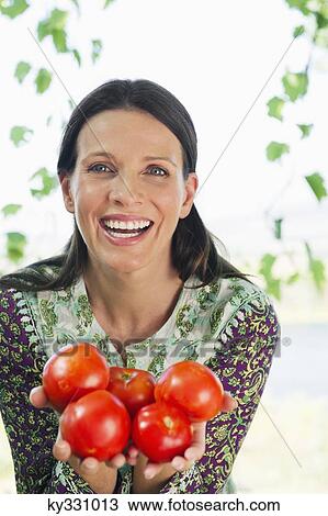 Stock Image - Portrait of a smiling mature woman holding tomatoes. Fotosearch