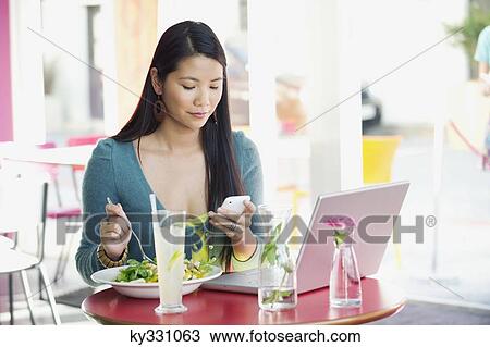 Stock Image - Woman reading text message while eating food in a restaurant. Fotosearch