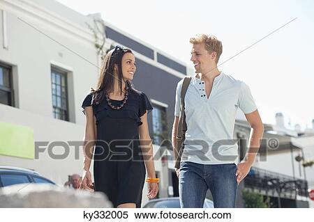 Smiling young couple looking at each other while walking View Large Photo Image Stock Photography - Smiling young couple looking at each other while walking. Fotosearch