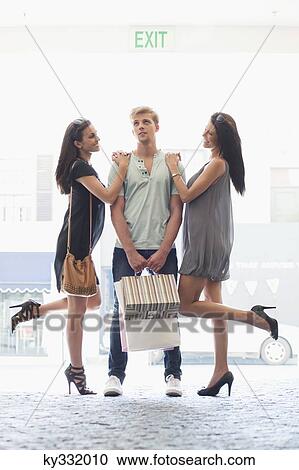 Stock Image - Two young women standing with hands in man's shoulders. Fotosearch
