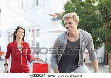Young man cycling with his girlfriend running after him with shopping bags View Large Photo Image Picture - Young man cycling with his girlfriend running after him with shopping bags. Fotosearch