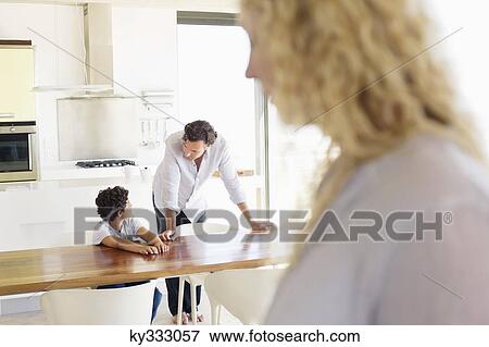 Stock Photo - Close-up of a woman with focus on father and son talking to each other in the background. Fotosearch