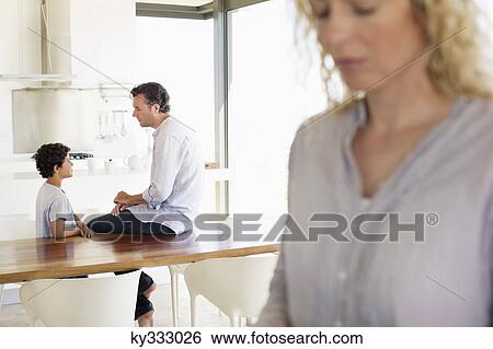 Stock Photograph - Close-up of a woman with focus on father and son talking to each other in the background. Fotosearch