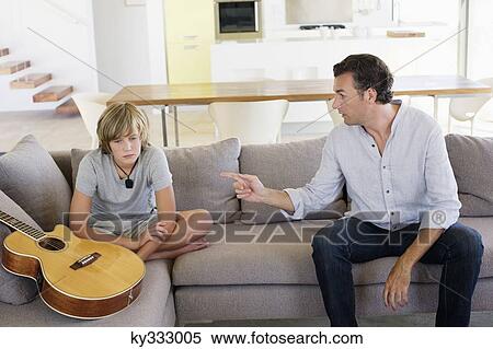 Stock Photography - Father complaining to teenage boy sitting with guitar at home. Fotosearch