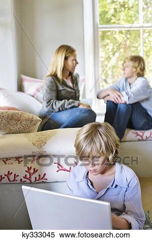 Little boy using laptop with family members talking in the background View Large Photo Image Stock Photography - Little boy using laptop with family members talking in the background. Fotosearch