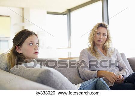 Mid adult woman and her daughter sitting on a couch View Large Photo Image Stock Image - Mid adult woman and her daughter sitting on a couch. Fotosearch