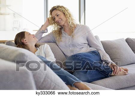 Stock Photograph - Mid adult woman and her daughter sitting on a couch and smiling. Fotosearch