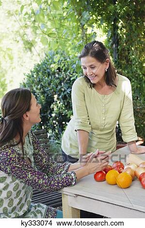 Senior woman talking to her daughter with vegetables on table View Large Photo Image Picture - Senior woman talking to her daughter with vegetables on table. Fotosearch