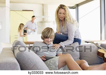 Stock Image - Teenage boy using a digital tablet with his mother looking at him. Fotosearch