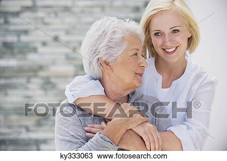 Young woman embracing her mother from behind and smiling View Large Photo Image Stock Image - Young woman embracing her mother from behind and smiling. Fotosearch