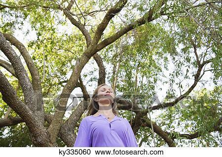 Stock Image - Young woman standing under a tree. Fotosearch