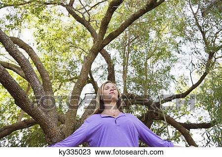 Young woman standing under a tree with her eyes closed View Large Photo Image Stock Image - Young woman standing under a tree with her eyes closed. Fotosearch