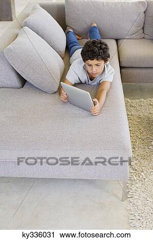 Stock Image - Boy lying on a couch and using a digital tablet. Fotosearch